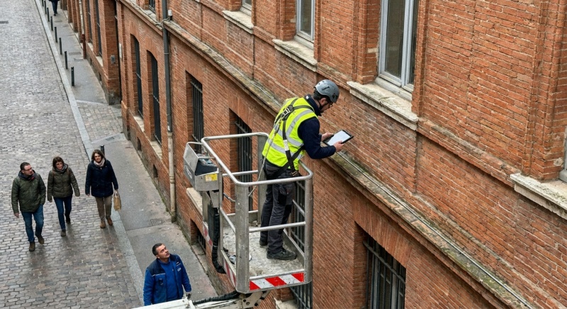 Technicien réalisant un audit technique sur une façade en briques rouges typique de Toulouse